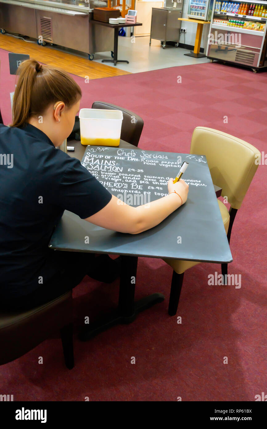 A young woman in a popular Garden Centre Café in North Yorkshire, writing out the Chef’s Special Lunch time menu for display on a blackboard. Stock Photo