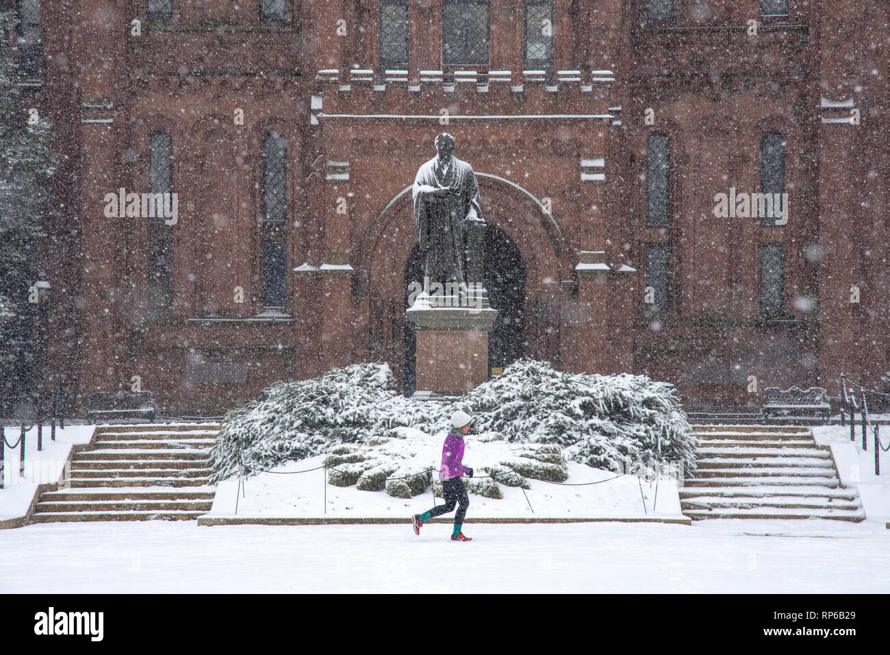 Snow-covered statue of Joseph Henry seems to watch a jogger run by the Smithsonian Castle, on the National Mall in Washington DC. Stock Photo