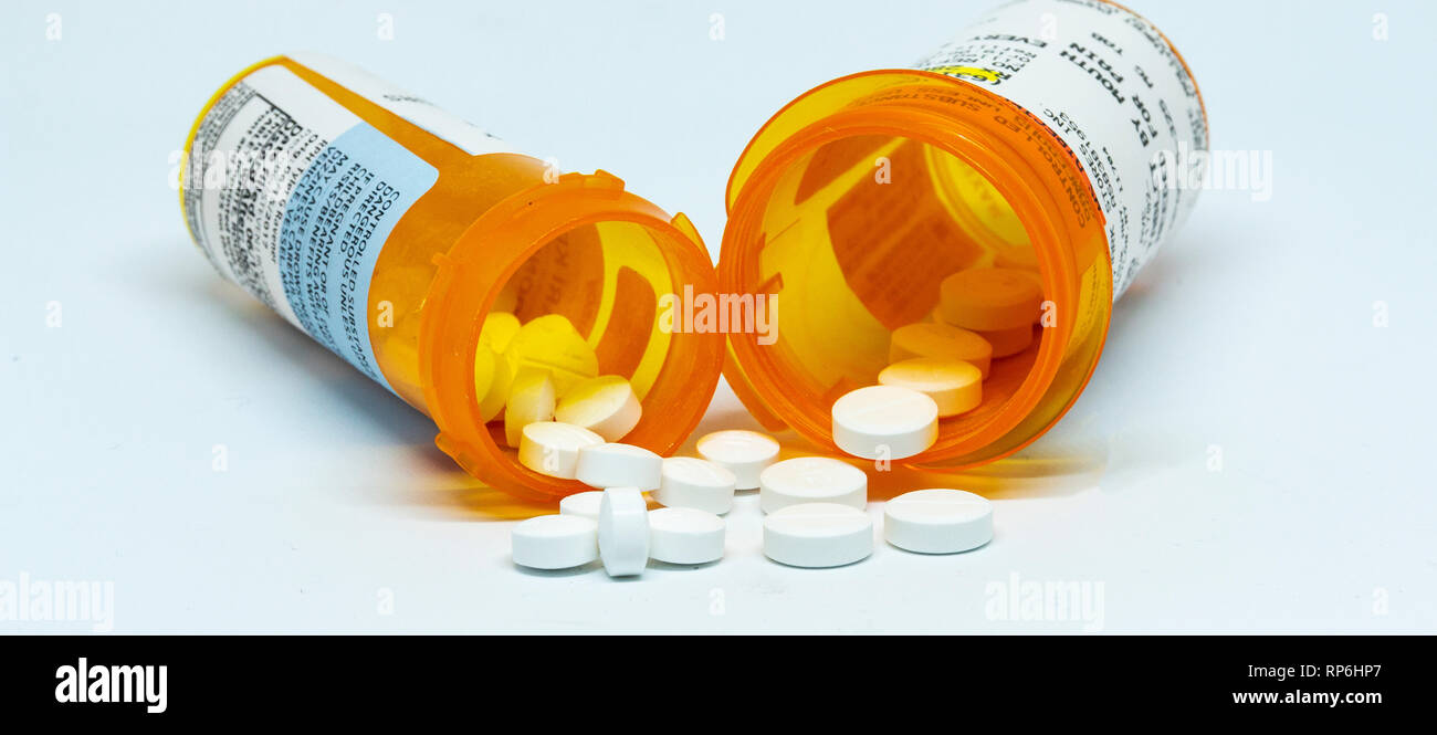 Two prescription bottles with pain pills spilling out of them with a white background. Stock Photo