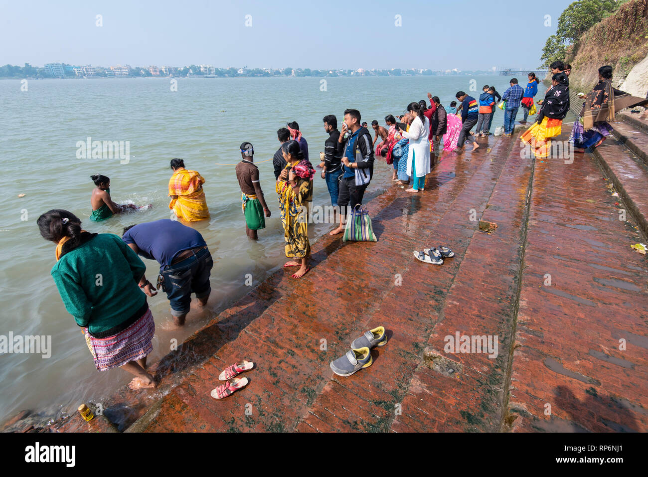 The Dakshineswar Kali Temple Ghat on the banks of the Hooghly River with local people bathing and washing on a sunny day with blue sky. Stock Photo