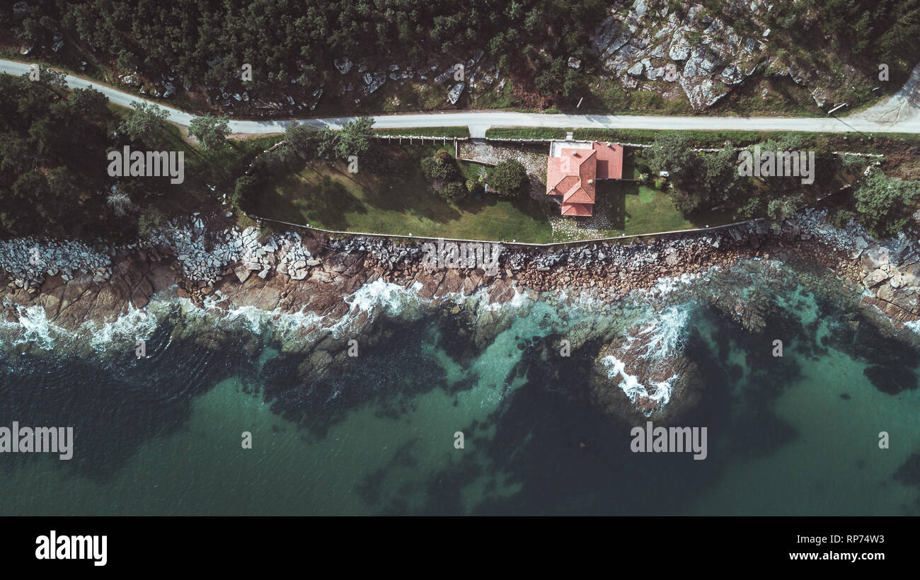 Drone aerial view of remote residential house on rocky beach in Galicia on a sunny bright day. Stock Photo