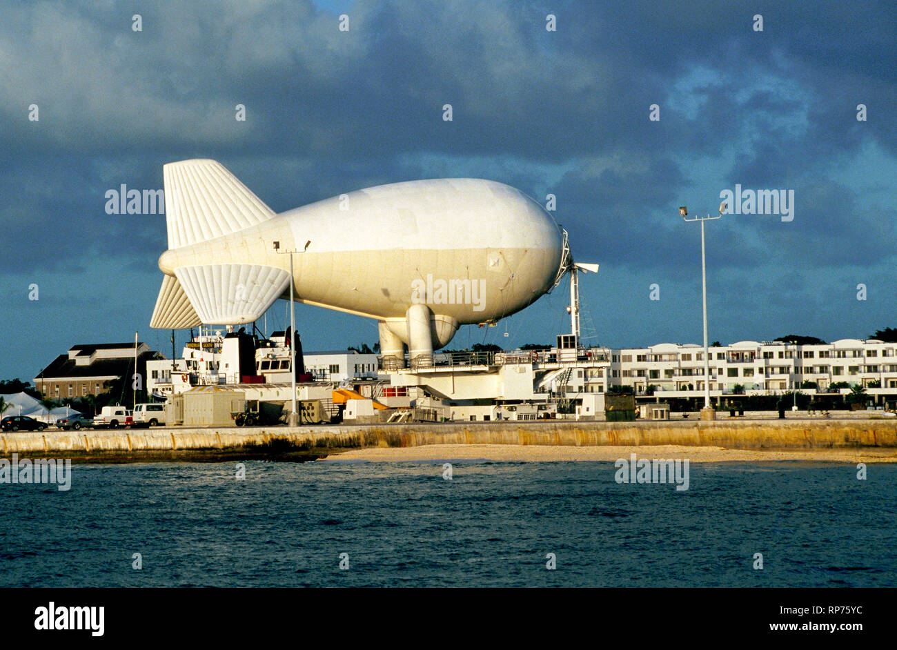 A helium-filled airship that carries aerial radar to detect drug-smuggling and other illegal activities is tethered to a ship at a U.S. Navy dock in Key West, Florida, USA. Officially called an aerostat, the big balloon is locally known as 'Fat Albert' and began operating in the area between the Florida Keys and Cuba in the 1980s. Tethered by a single cable, the unmanned blimp can be floated up to an altitude of 15,000 feet (4672 meters) and give radar coverage over 200 nautical miles (370 kilometers). It is now one of eight aerostats providing surveillance along America's southern border. Stock Photo