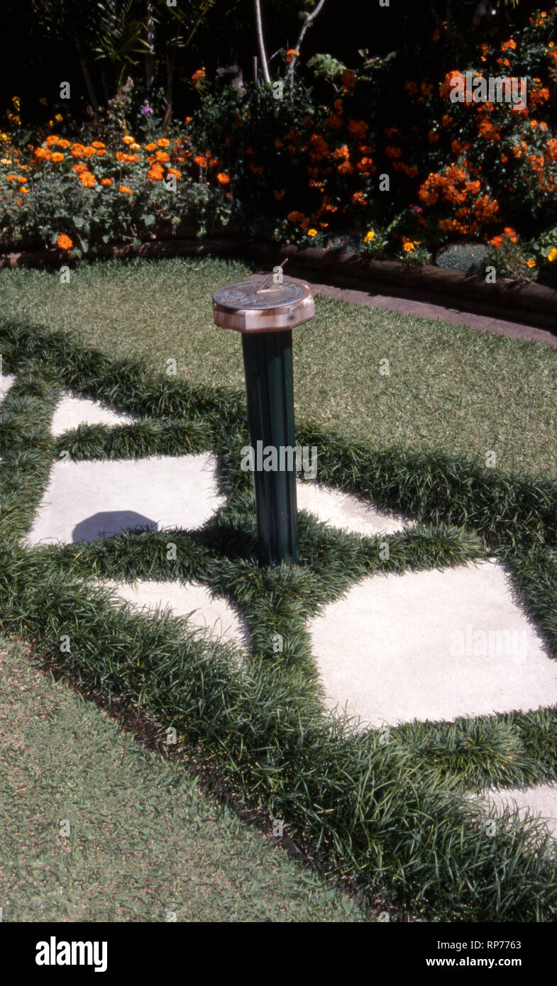 MONDO GRASS (OPHIOPOGON) GROWING ALONGSIDE PATH AND IN BETWEEN THE PAVERS.  SUNDIAL AS CENTRE PIECE, SUBURBAN GARDEN, NEW SOUTH WALES, AUSTRALIA. Stock Photo