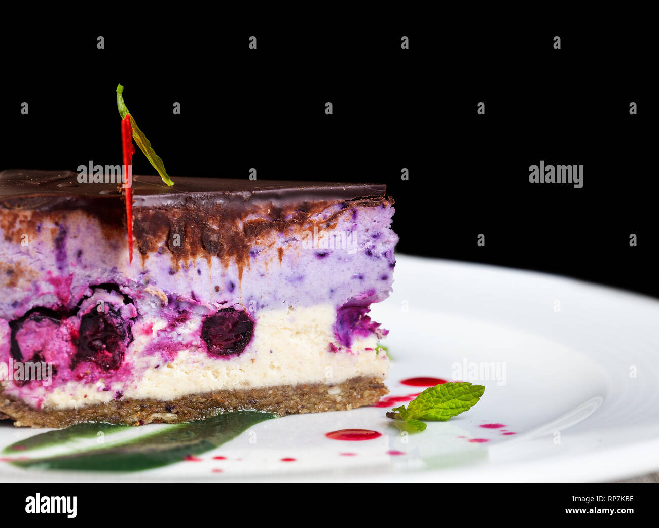 Raw vegan cake with berries decorated by chef on white plate closeup in restaurant at black background Stock Photo