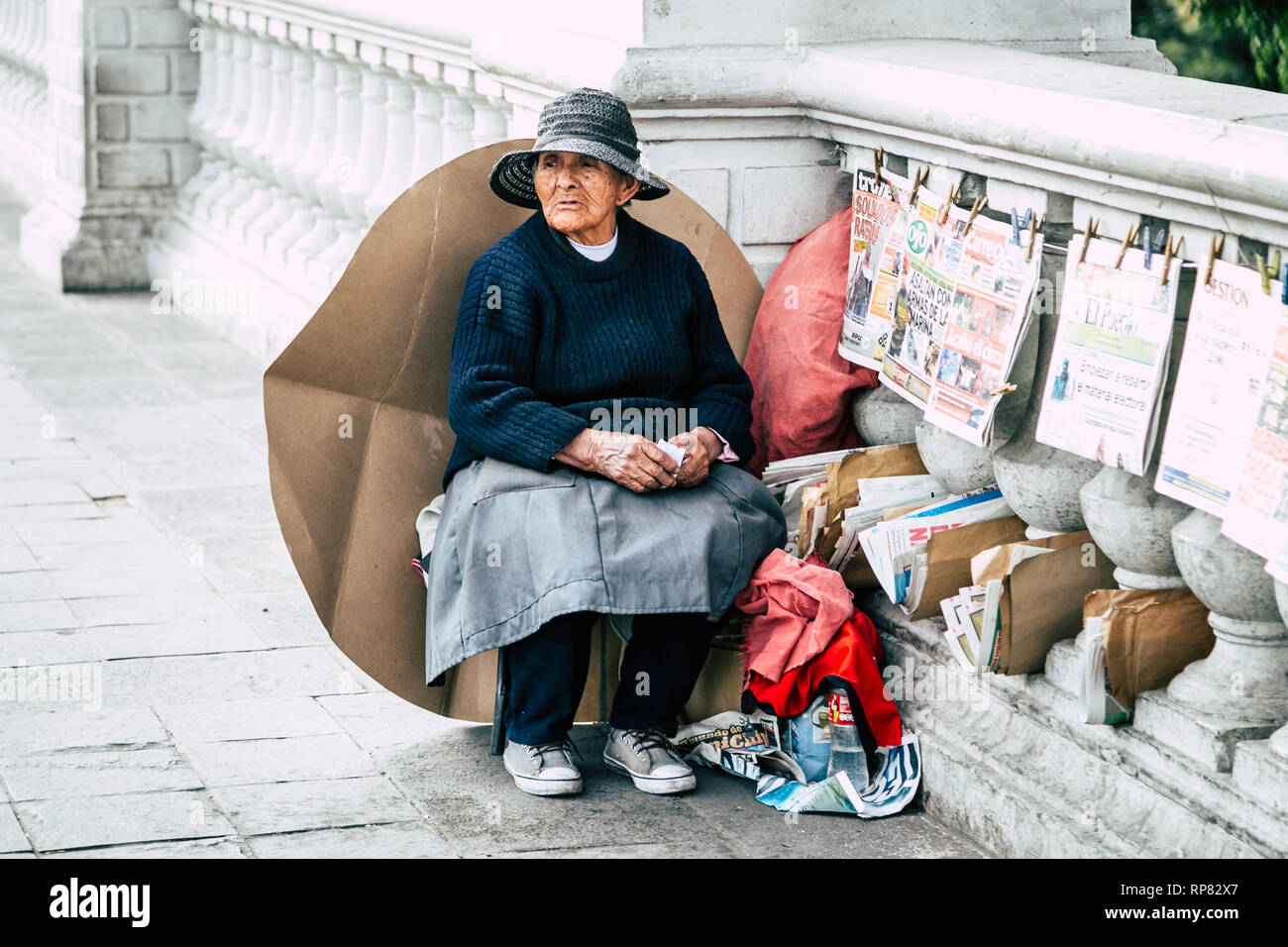 An elderly Peruvian woman - street vendor selling newspapers - sits on a colonial style bridge in Arequipa, Peru. Stock Photo