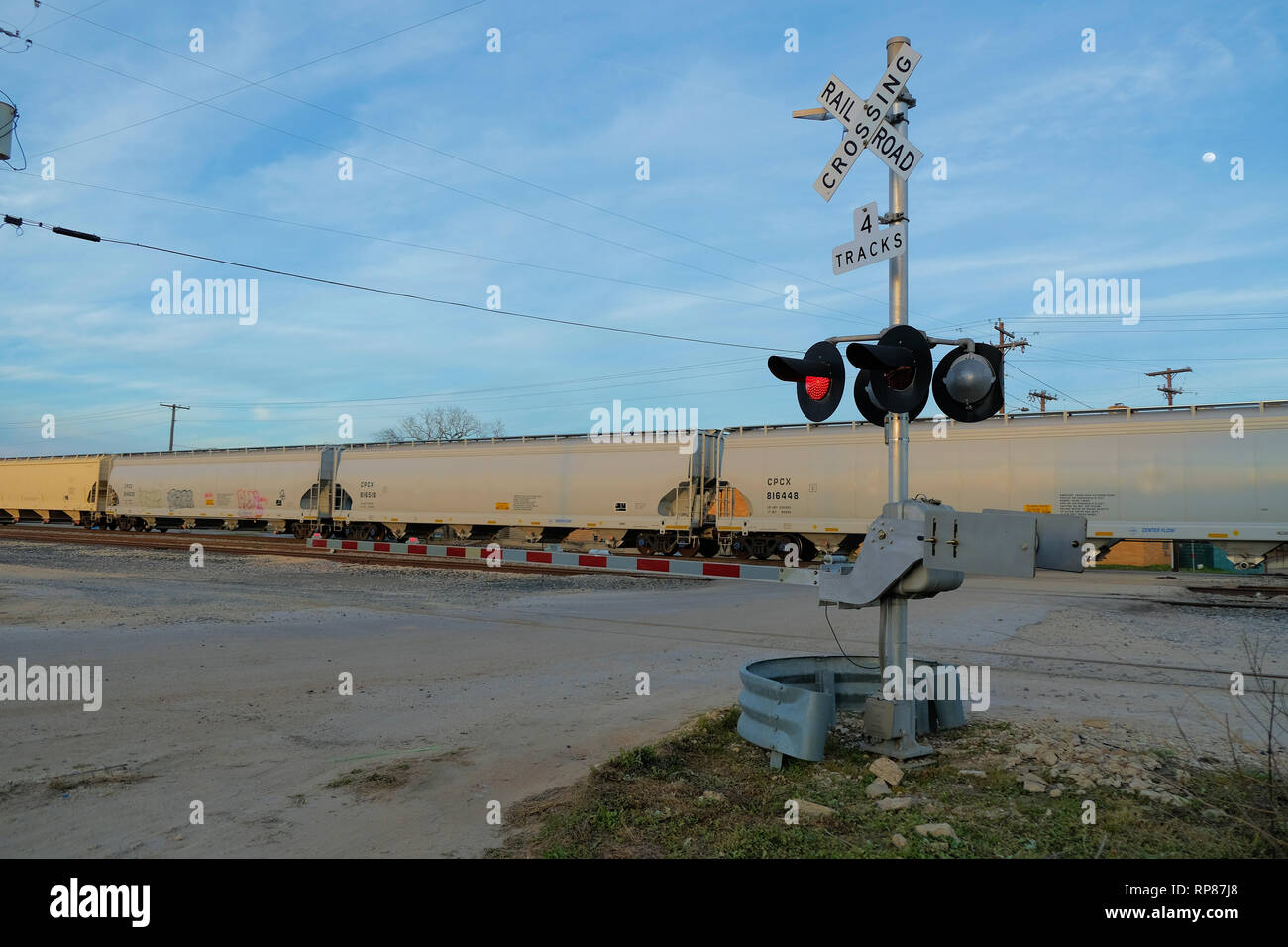 Railway boom barrier at a level railroad crossing with a train passing by in the background; four track railway crossing; Bryan, Texas, USA. Stock Photo