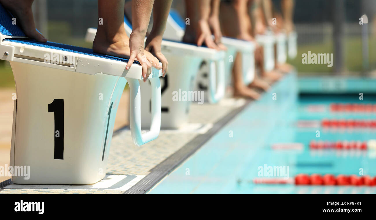 A line up of swimmers preparing to jump of the starting blocks in a swimming competition. Diving blocks focus on hand and feet lane 1. Stock Photo