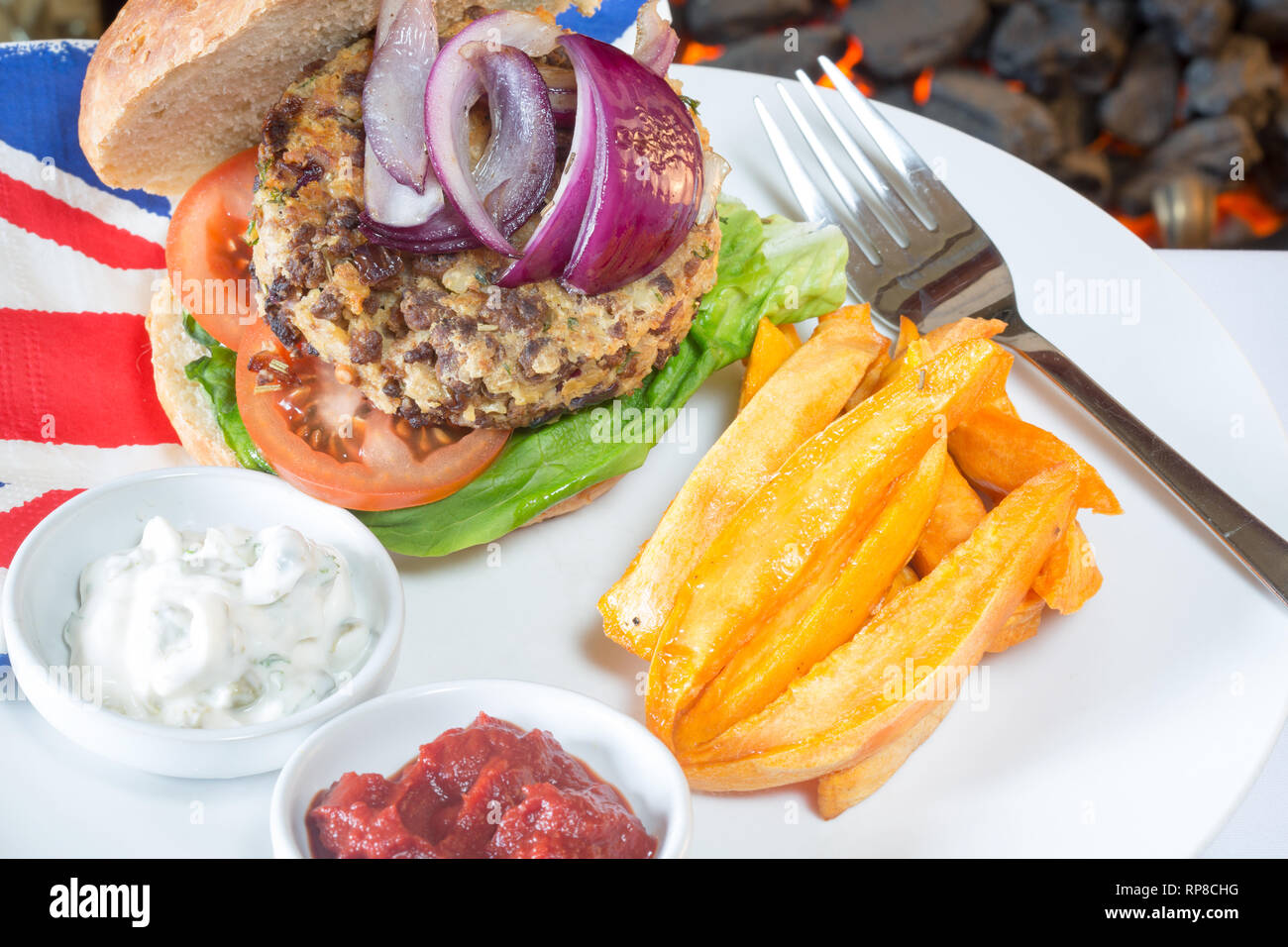 Homemade Quorn burger in a sourdough bun with lettuce, tomato, red onion, Sweet potato chips/fries, and served with ketchup and soy yogurt dips. Stock Photo