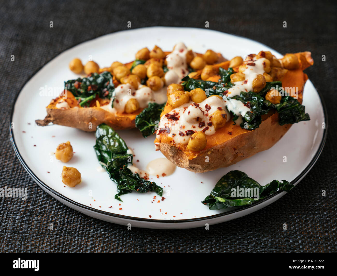Baked sweet potatoes loaded with spicy chickpeas and kale and a tahini Dressing. Stock Photo
