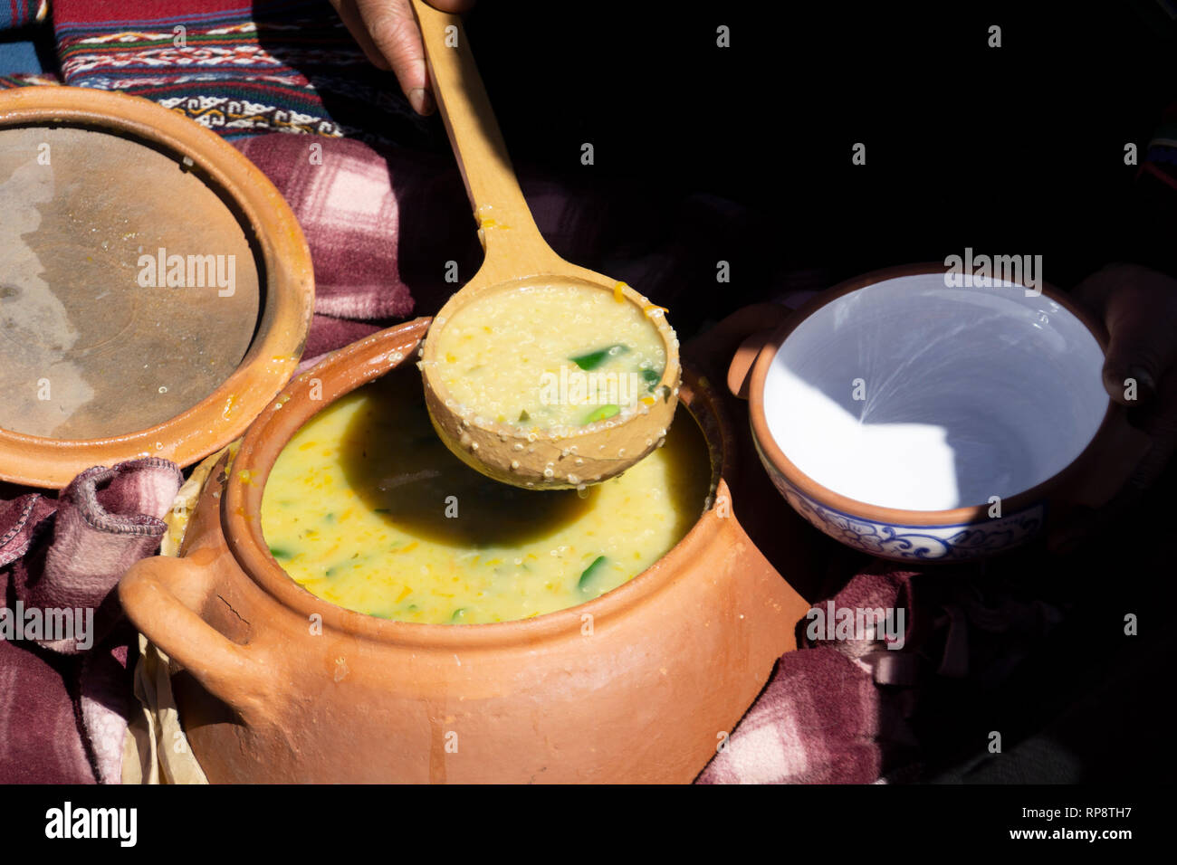 Serving traditional Incan potato soup from terra cotta clay urn pot with large round wooden spoon. Stock Photo