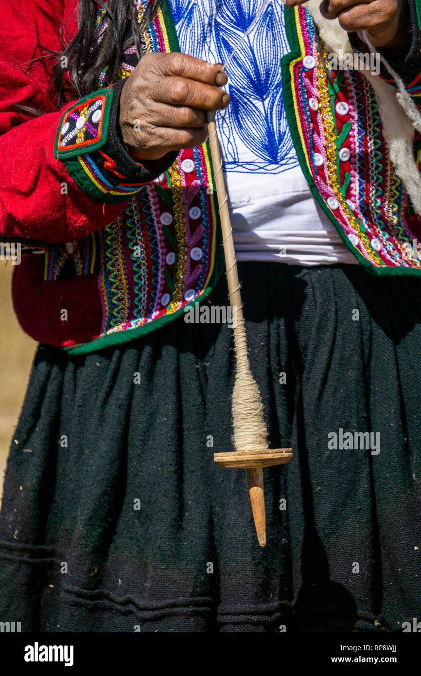 Woman in traditional dress spins alpaca wool yarn on spool in Sacred Valley, Cusco Region, Peru. Stock Photo