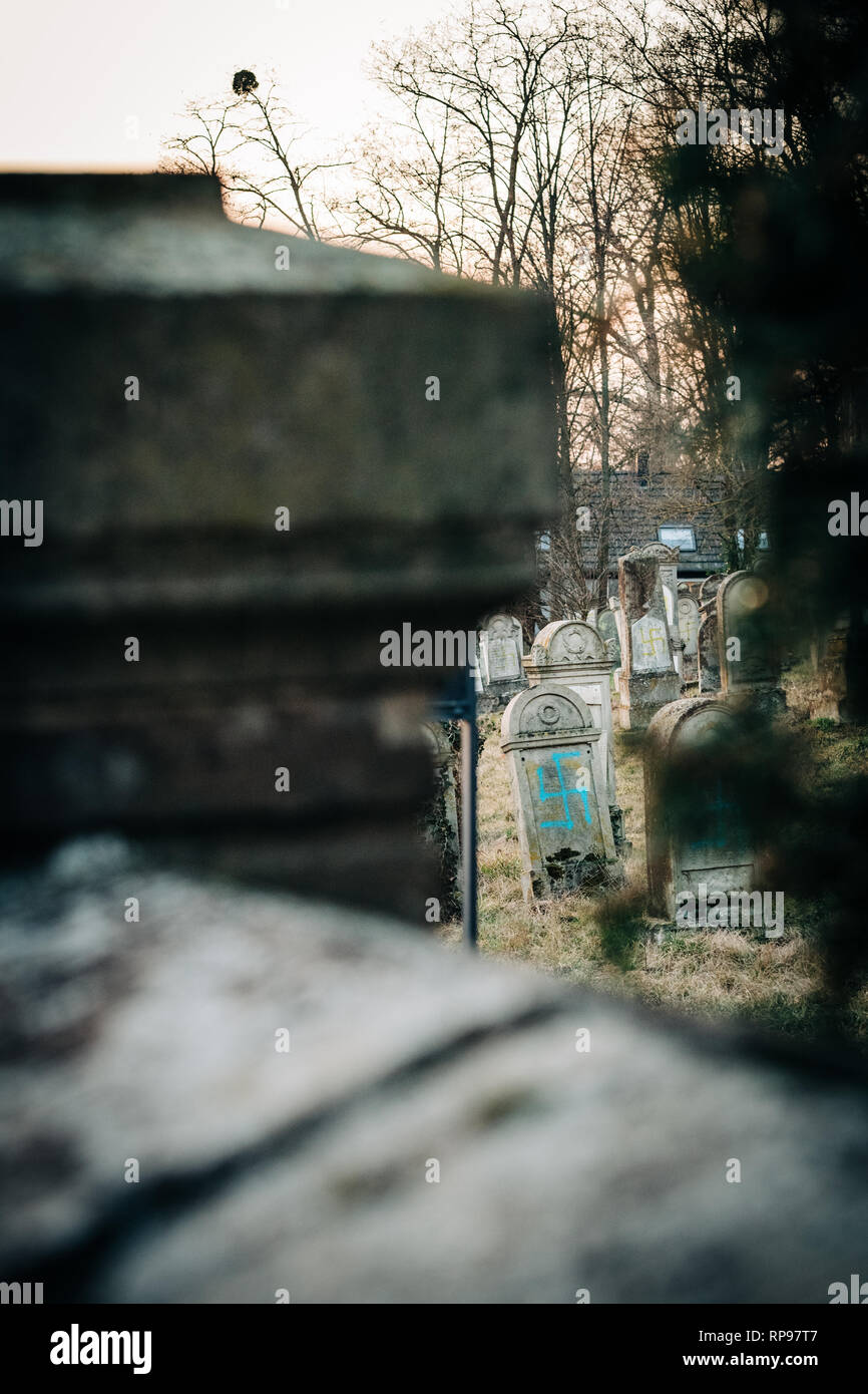 View though stones of multiple vandalised graves with nazi symbols in blue spray-painted on the damaged graves - Jewish cemetery in Quatzenheim near Strasbourg  Stock Photo