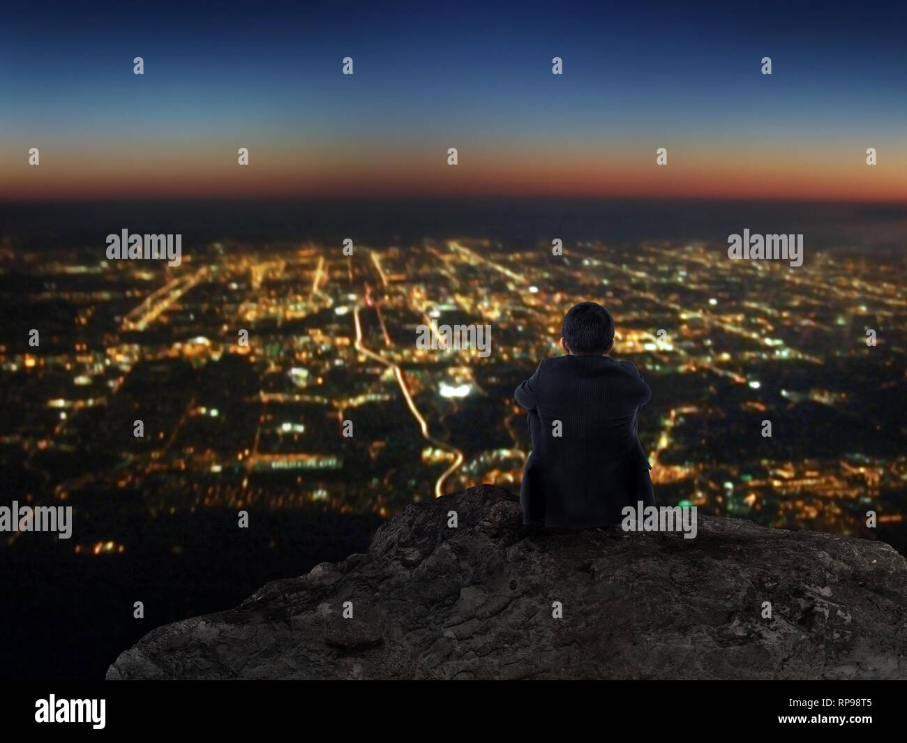 Businessman sitting on rock mountain with city view at night Stock Photo