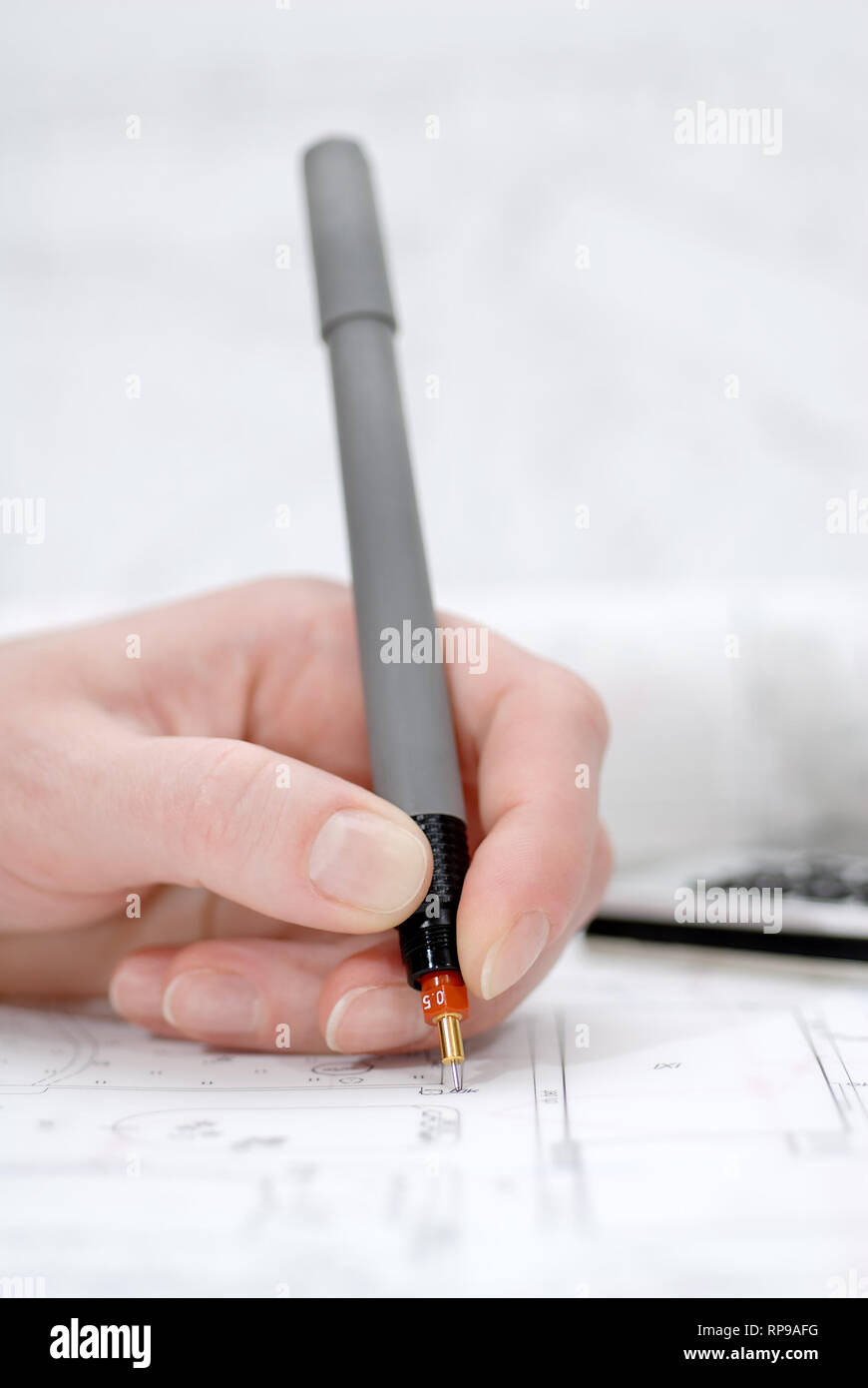 Woman's hand holding rapidograph, architectural plans in background Stock Photo