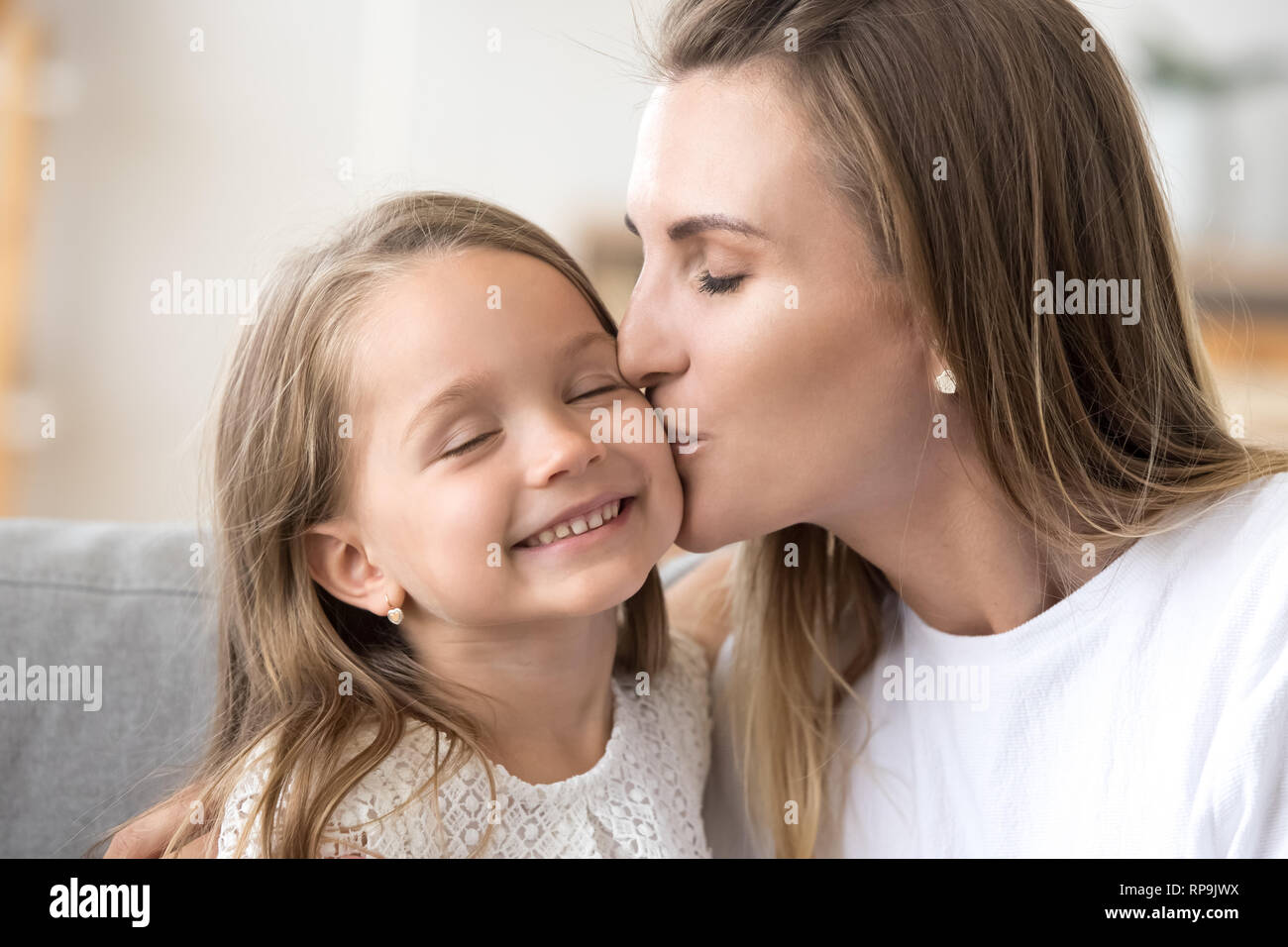 Loving young mother kissing little smiling daughter on cheek Stock Photo