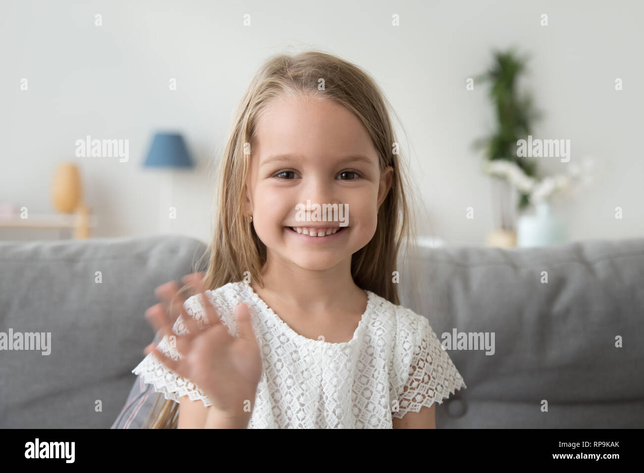 Smiling little girl looking at camera, waving hand, greeting Stock Photo