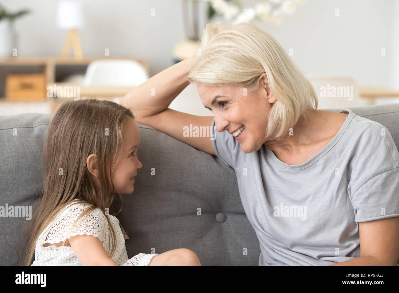 Little granddaughter talking with attentive grandmother, sitting on sofa Stock Photo