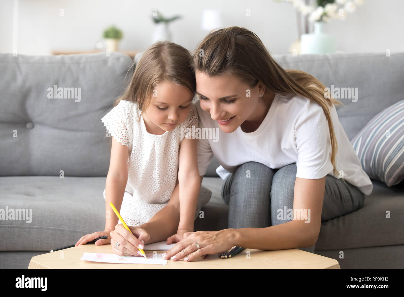 Smiling mother with preschool daughter drawing with colored pencils Stock Photo