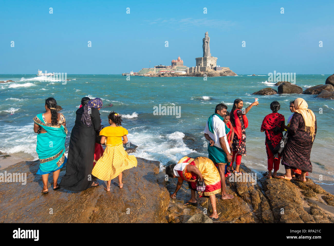 Tourists and local people on the shore of Kanyakumari looking at The Vivekananda Rock Memorial  and Thiruvalluvar Statue on a sunny day with blue sky. Stock Photo