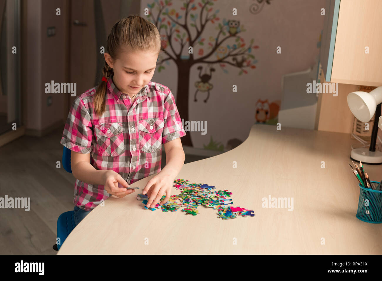 Cute little girl solving puzzle together sitting at the table Stock Photo