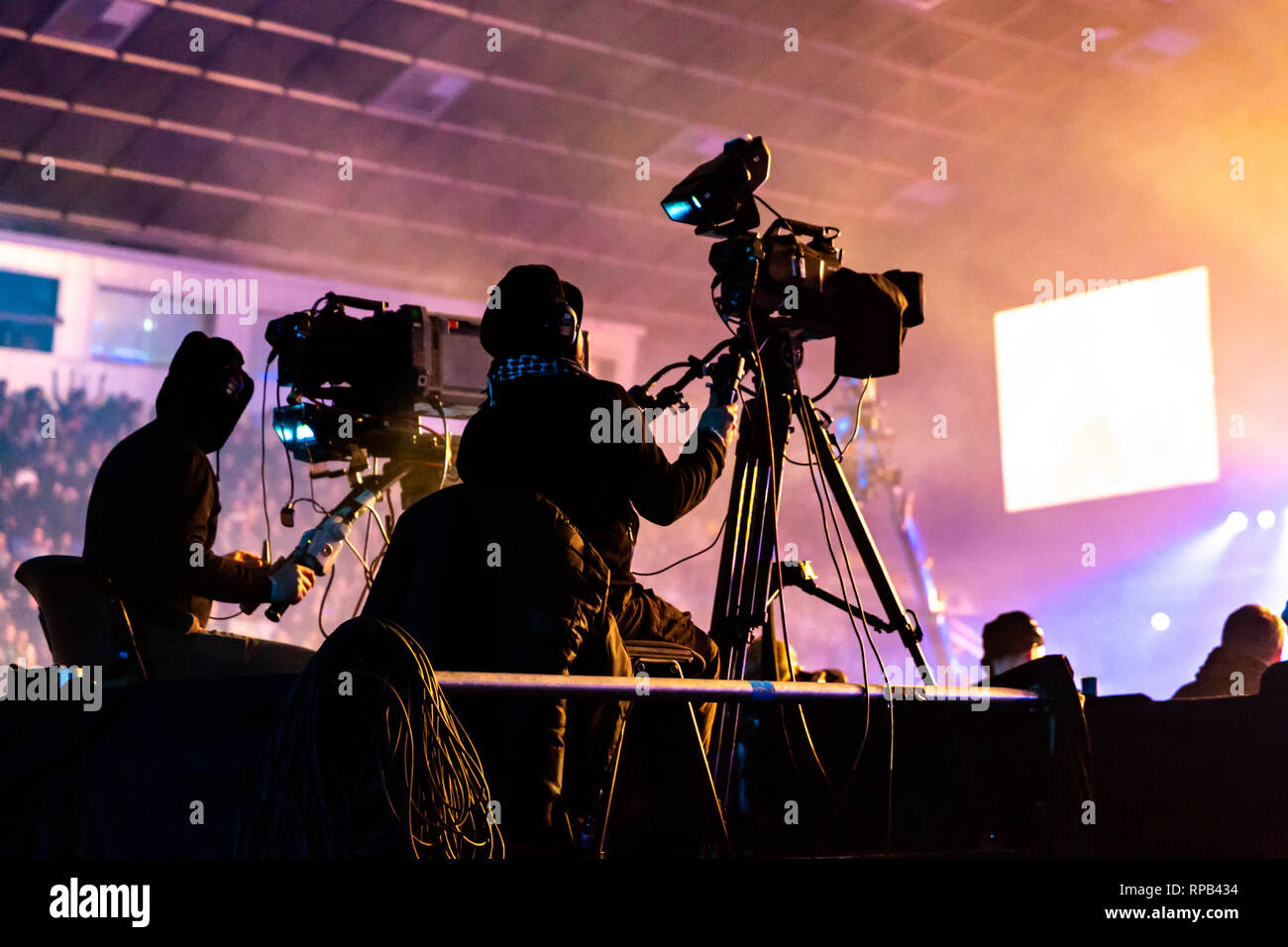 A group of cameramen working during the concert. Television broadcast event. Silhouettes of workers against the background of colorful beams. Stock Photo