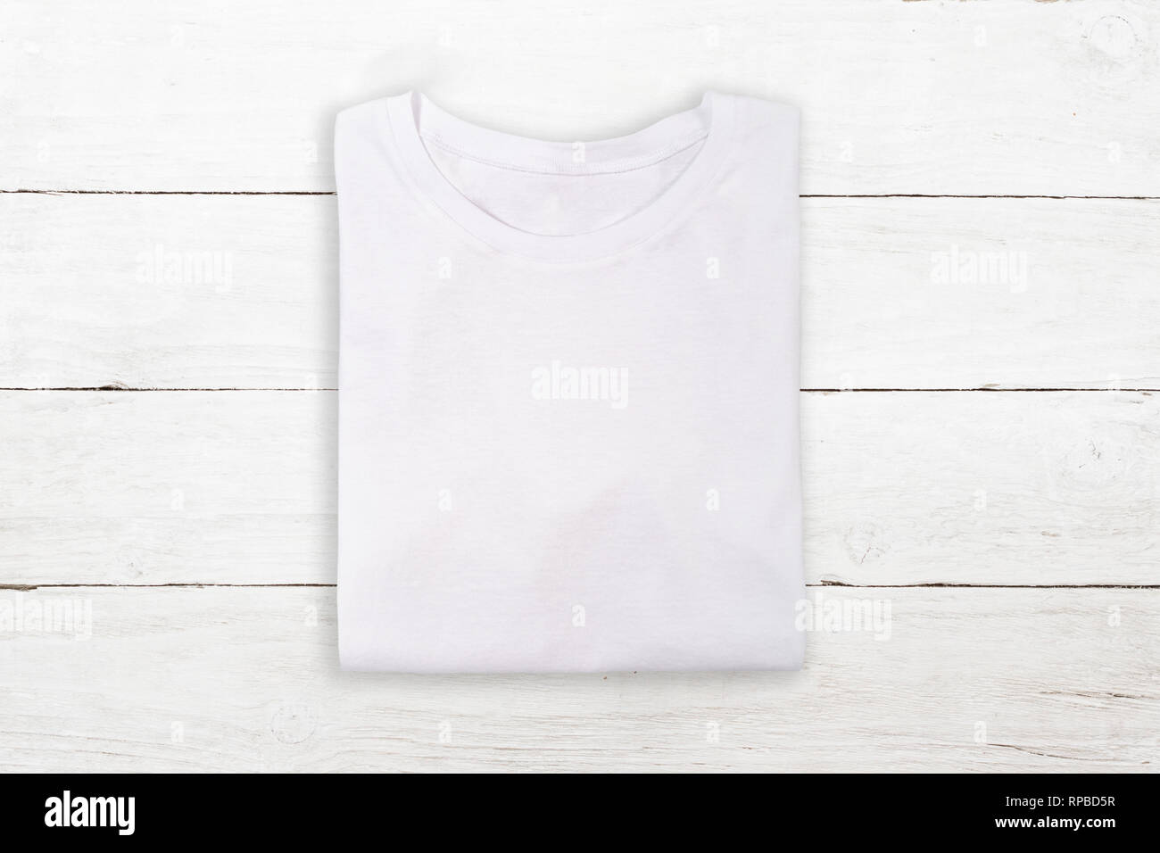 Above view of white folded t-shirt on white wooden background Stock Photo