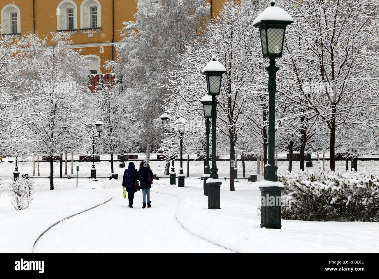Snowfall in Moscow, people walking in Alexander garden during blizzard. Winter landscape with snow covered vintage lanterns and trees, cold weather Stock Photo