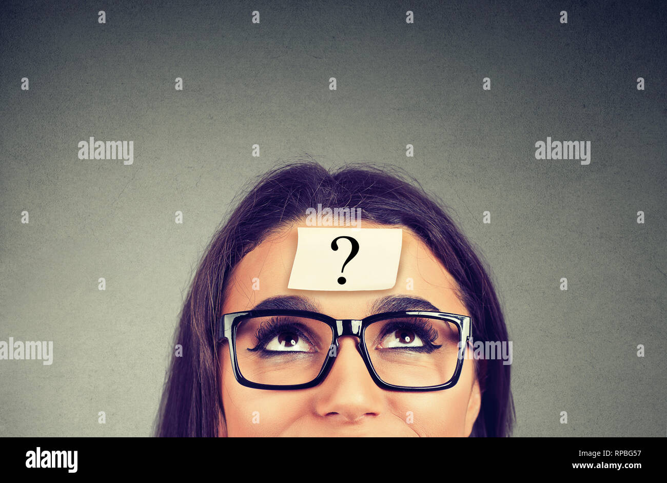 thinking woman in glasses with question mark looking up on gray wall background Stock Photo