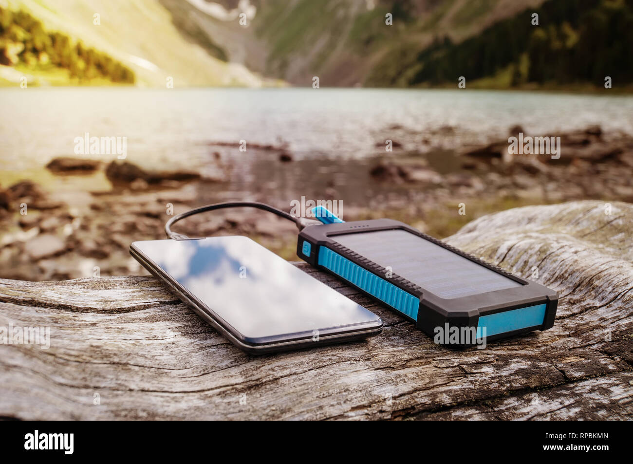 Portable solar panel for charging mobile devices lying on a log in the mountains where there is no electricity Stock Photo
