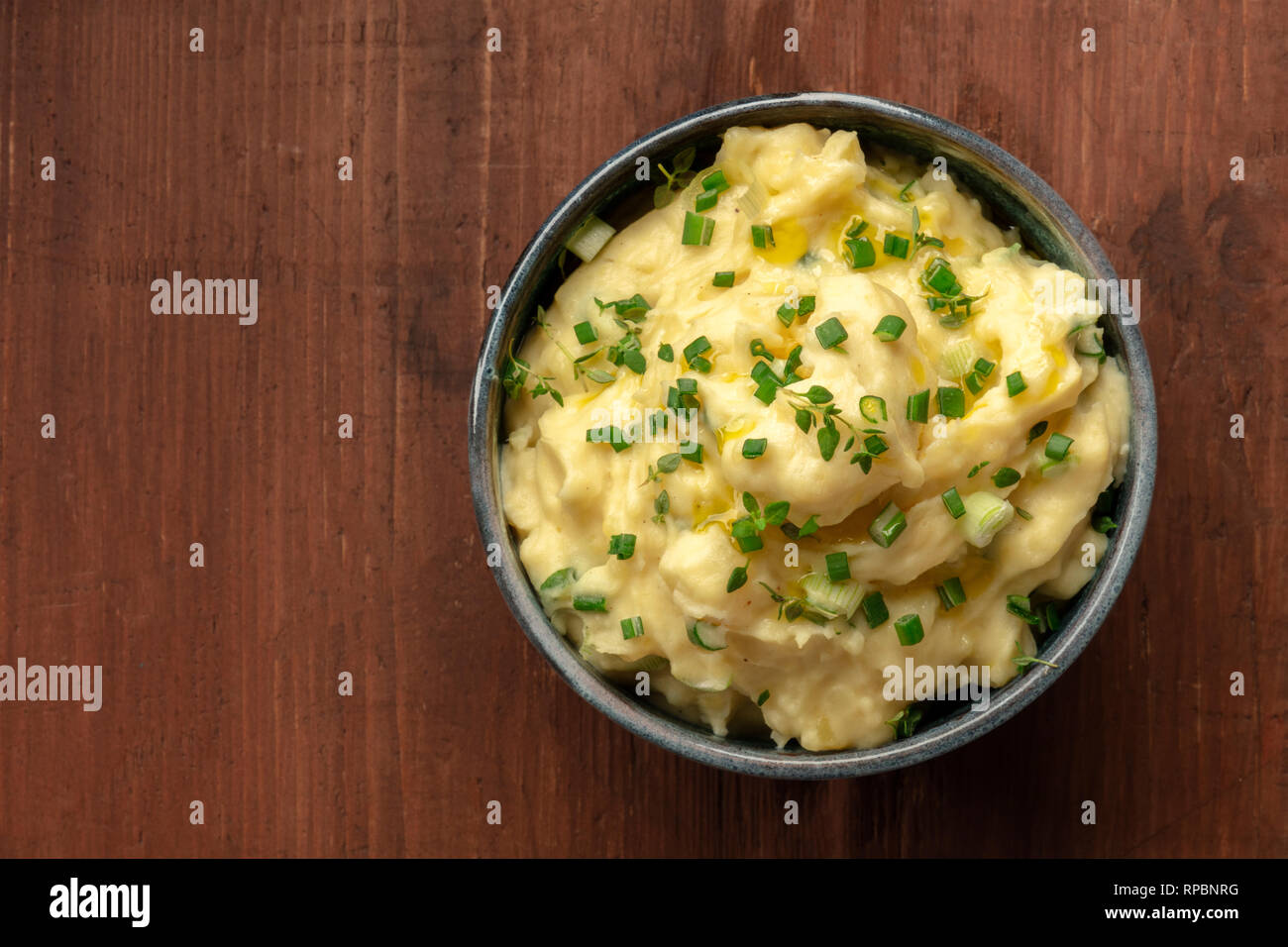 Pomme puree, a bowl of mashed potatoes with scallions and thyme, shot from above on a dark rustic wooden background with copy space Stock Photo