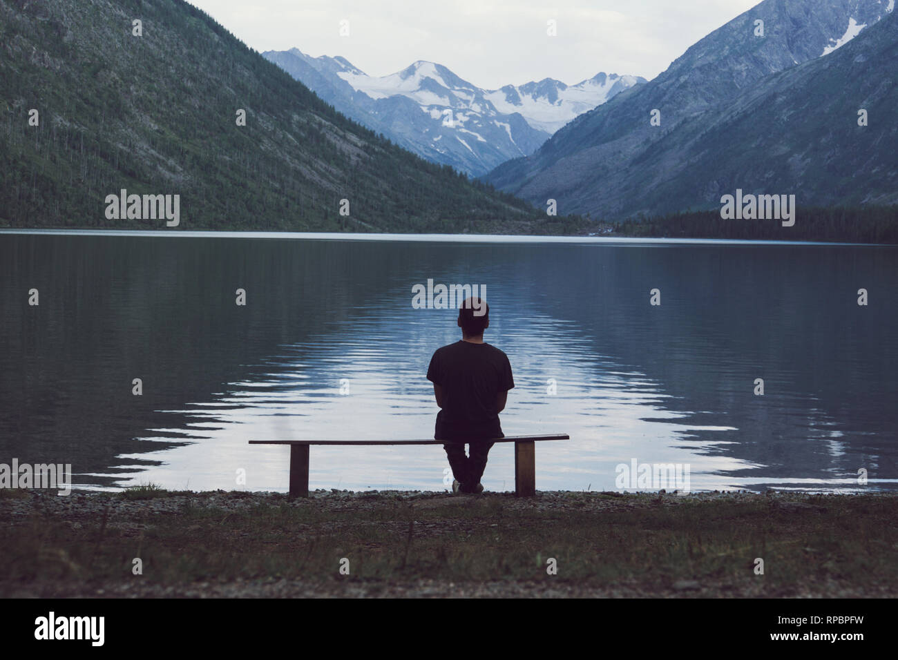 Man sitting on bench overlooking like. The concept of loneliness. Stock Photo