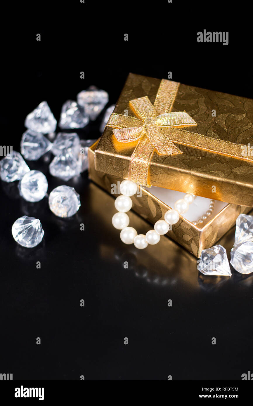 Golden jewellery box with white pearls and diamonds on a black glossy
