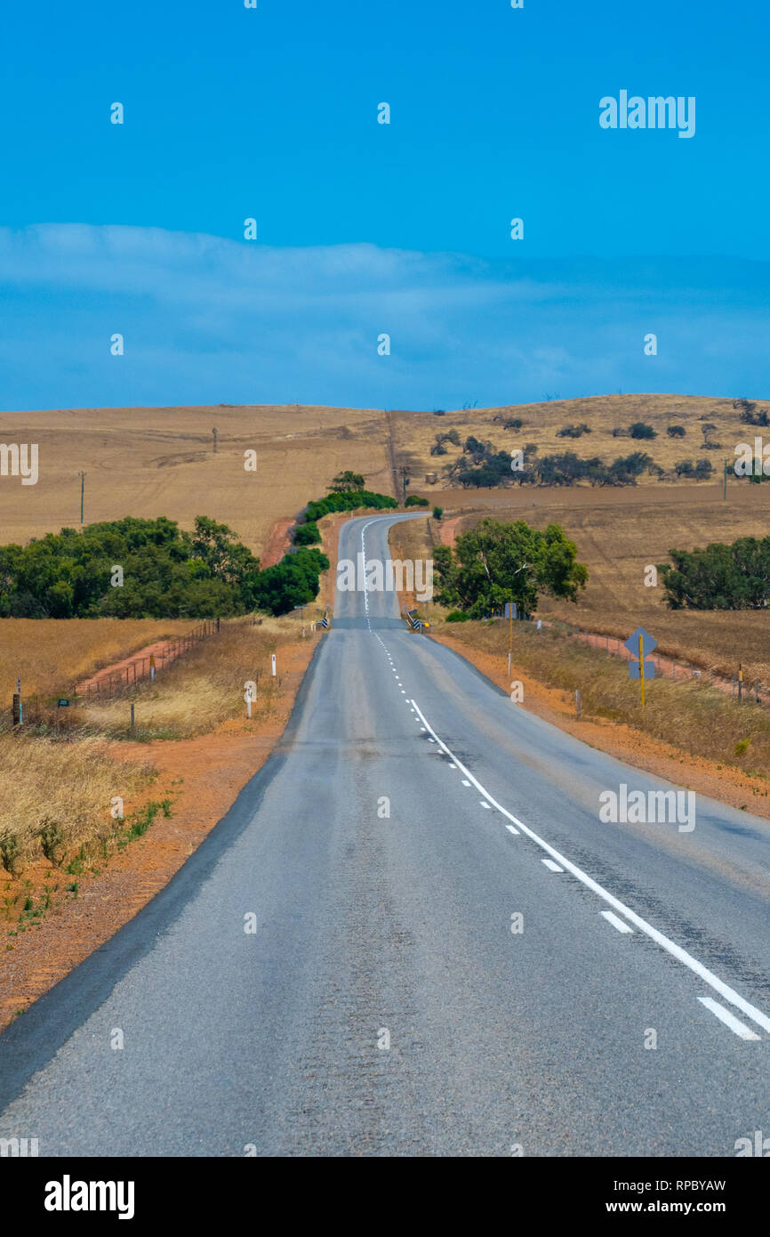 Australian bush road leading through dry landscape and farmland with