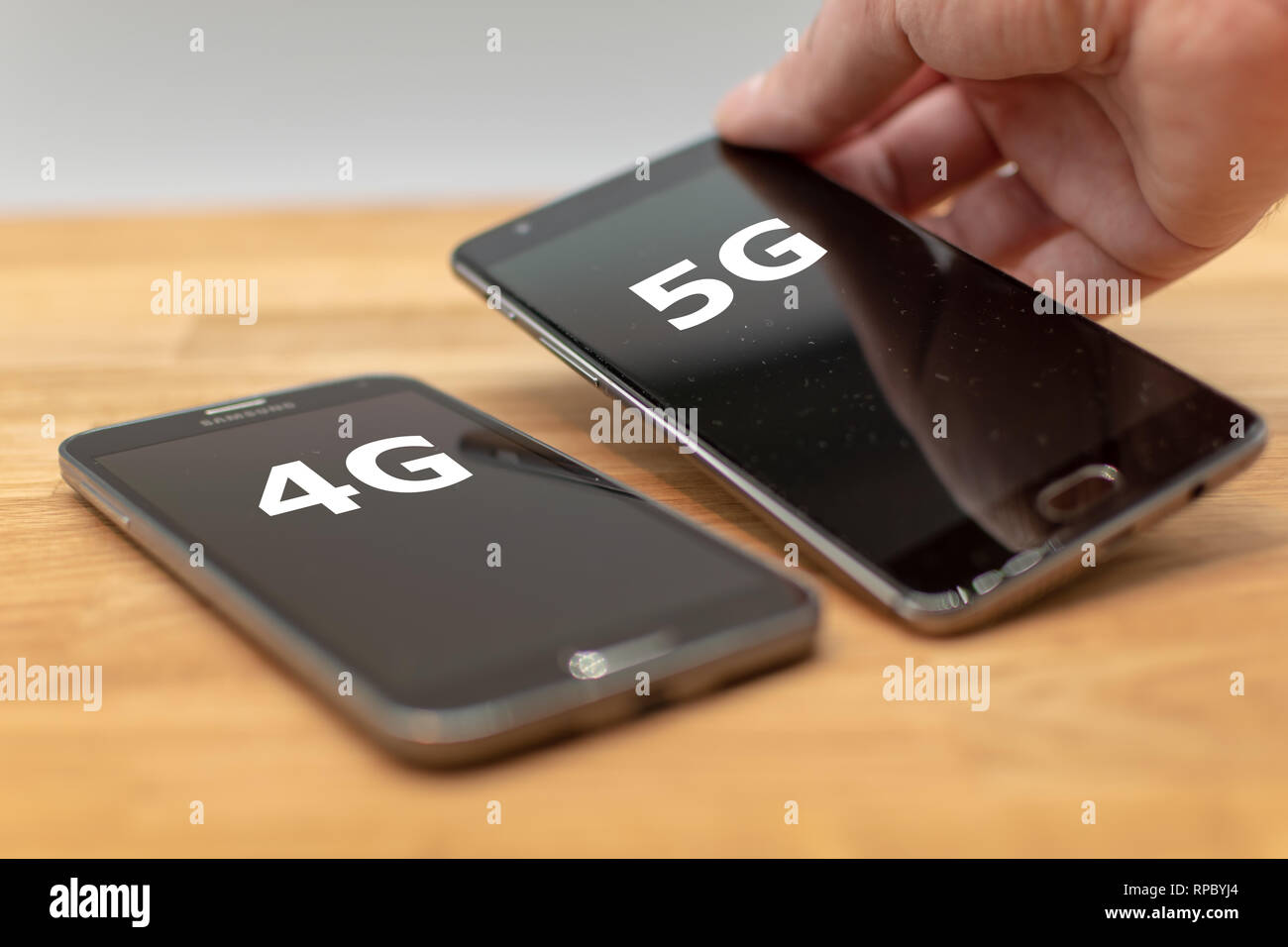 Two mobile phones on a wooden desk. Hand selects the phone with the label "5G" instead of the "4G" phone. Stock Photo