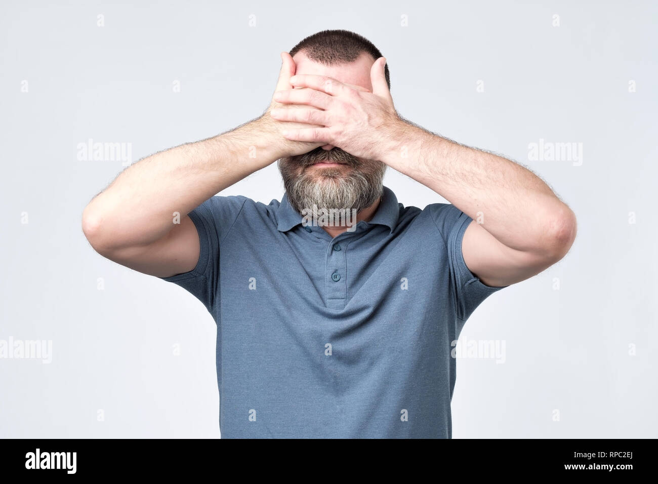 Man in blue t-shirt covering his face with hands Stock Photo