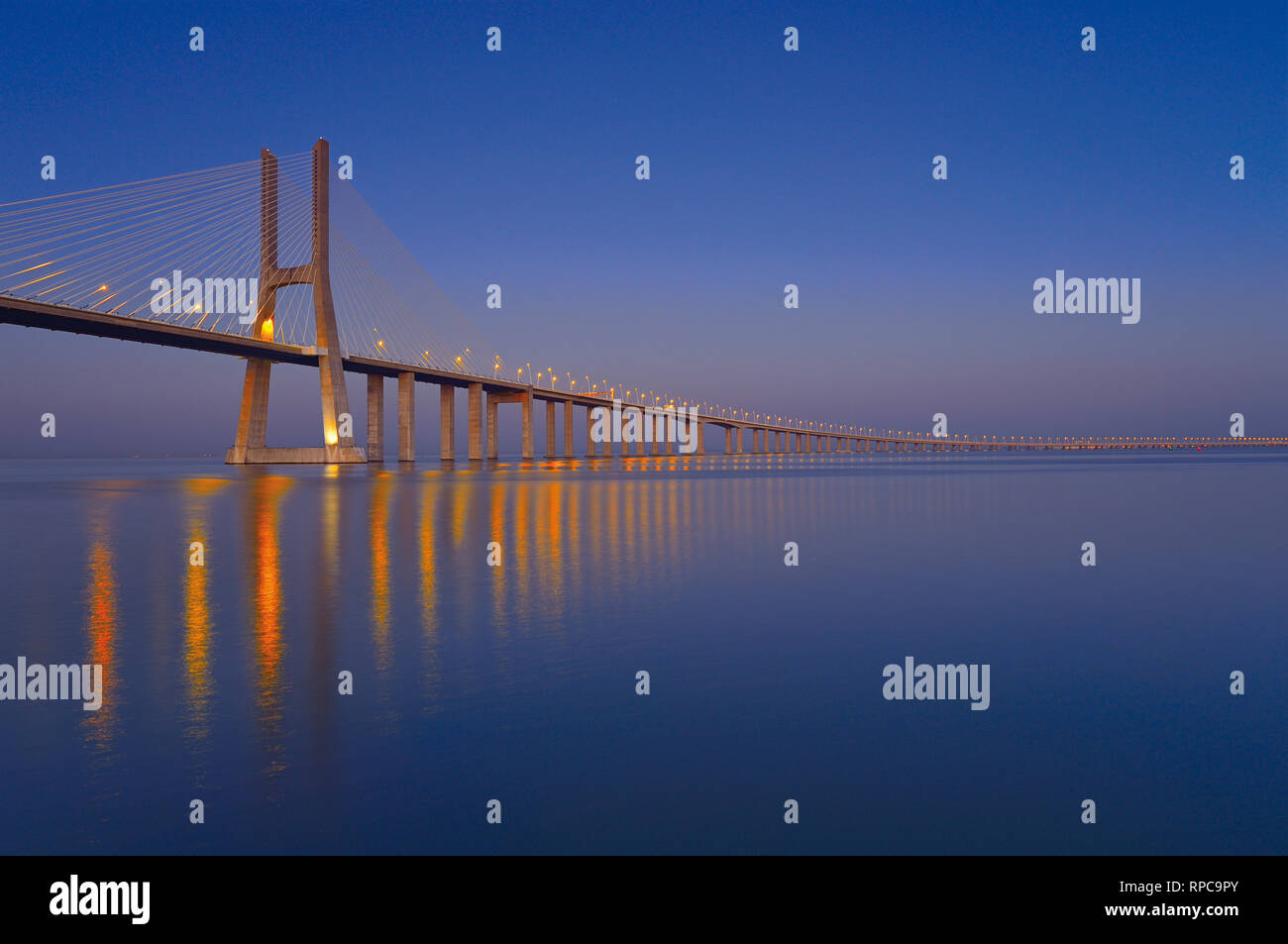 Elegant steel bridge at night passing kilometers over large calm river water Stock Photo