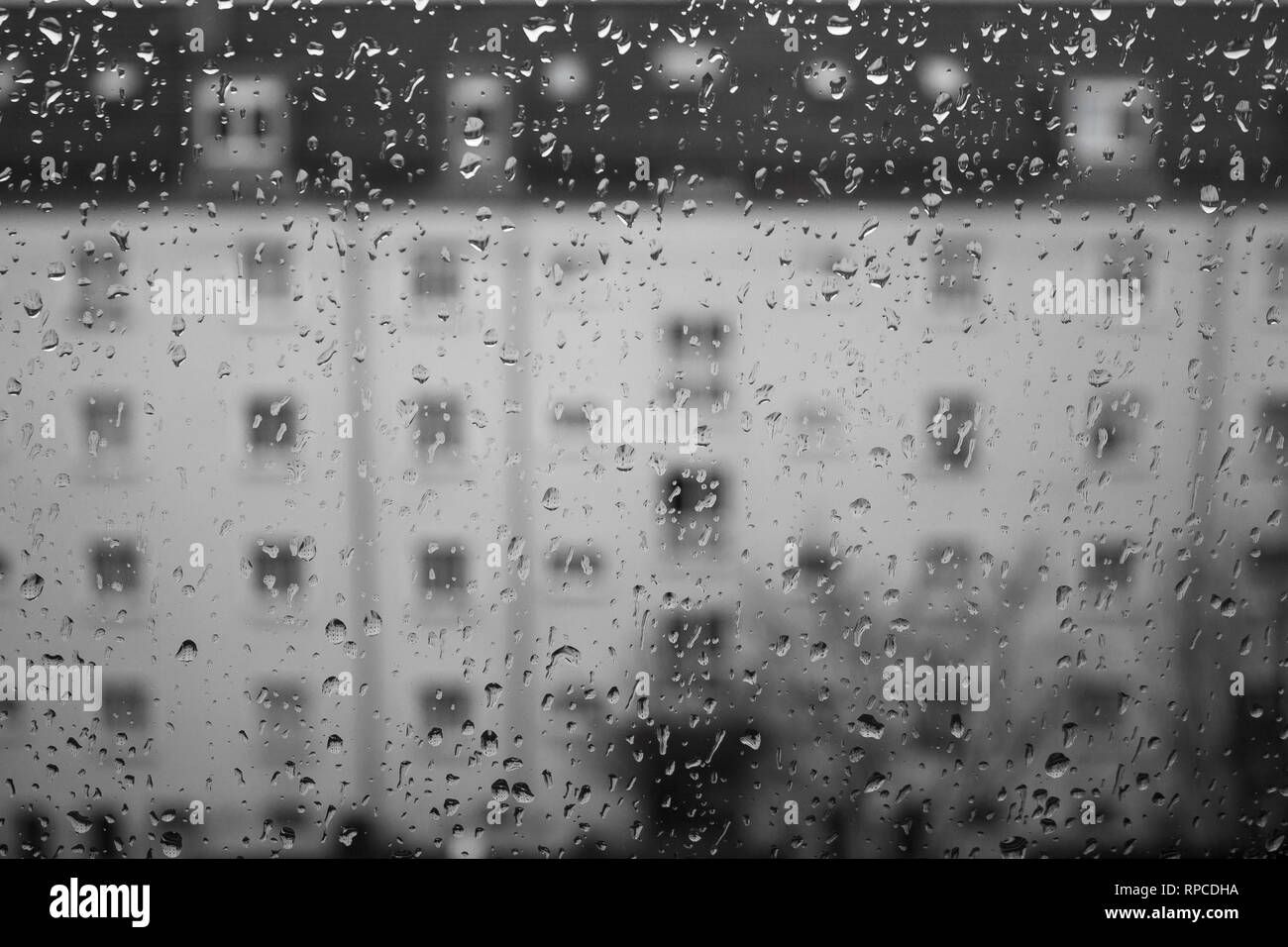 Drops of rain on glass , rain drops on clear window. Water condensation on transparent glass over city landscape or building in blur. Monochromatic Stock Photo