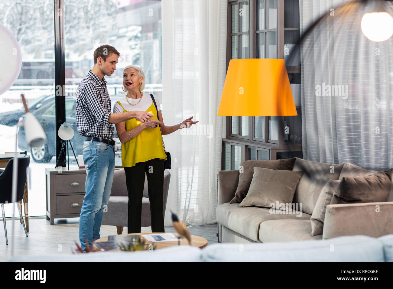 Handsome adult son discussing sofa purchasing with stylish elderly mom Stock Photo