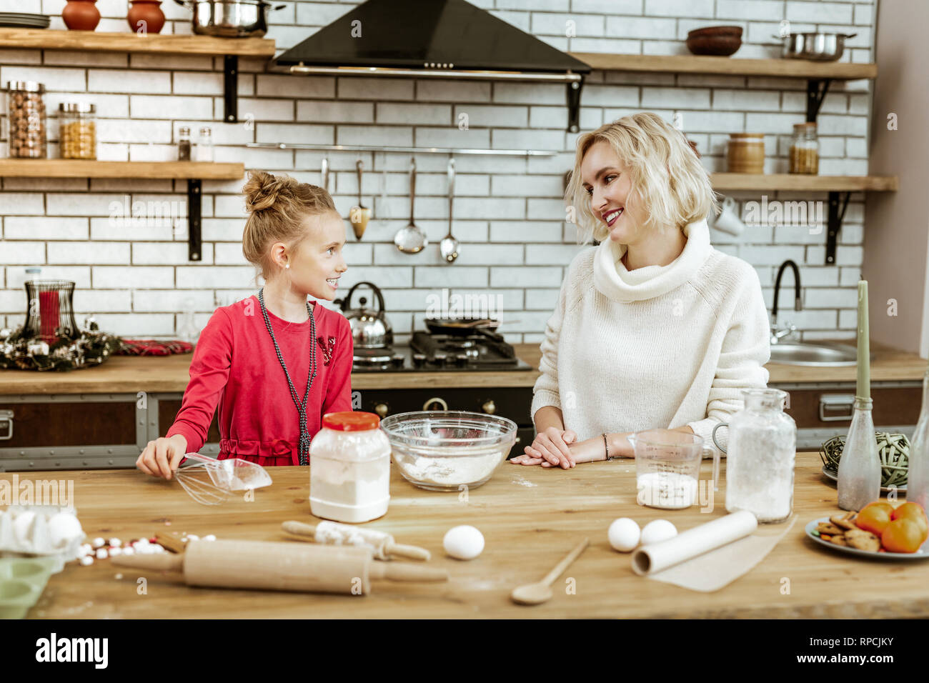 Beaming short-haired mother sitting on kitchen in white sweater Stock Photo