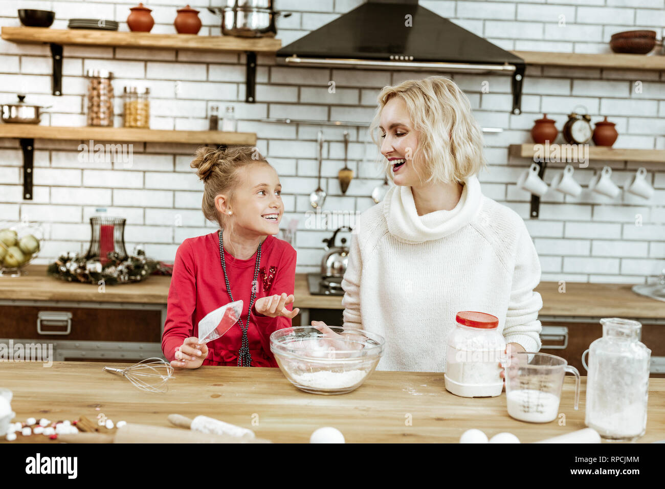 Laughing short-haired woman in oversize sweater listening to active child Stock Photo