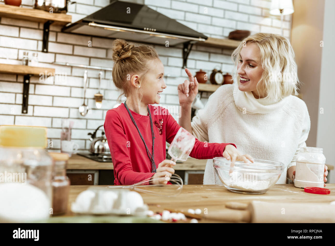 Amused good-looking blonde mother having fun with baking ingredients Stock Photo