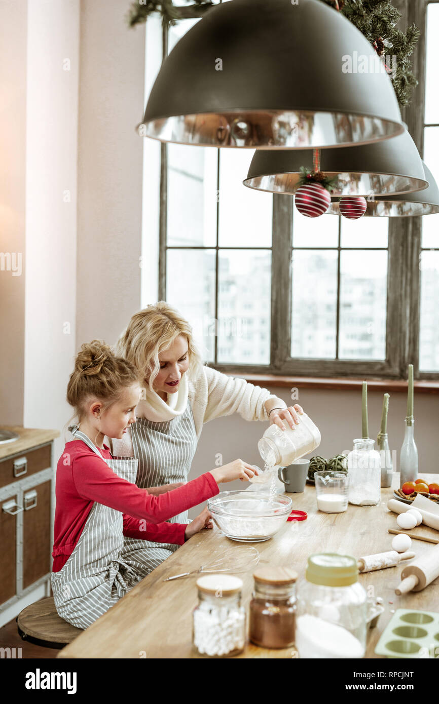 Mother and daughter wearing striped apron and cooking on wooden kitchen table Stock Photo