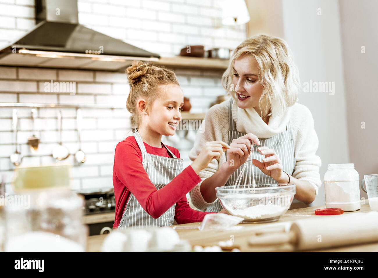 Smiling little kid in red dress asking about baking process Stock Photo