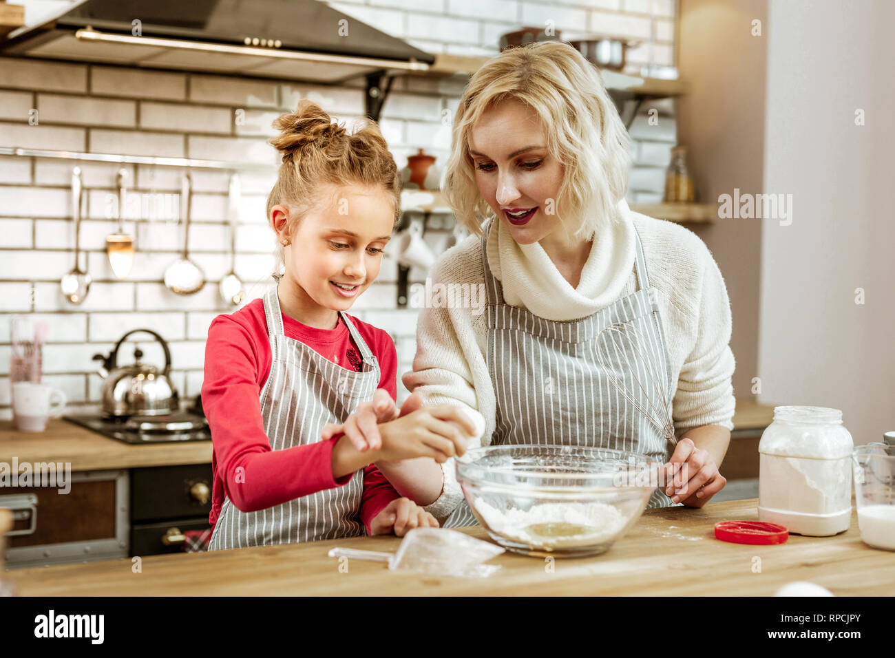 Attentive short-haired mother in apron showing her daughter process of cracking Stock Photo