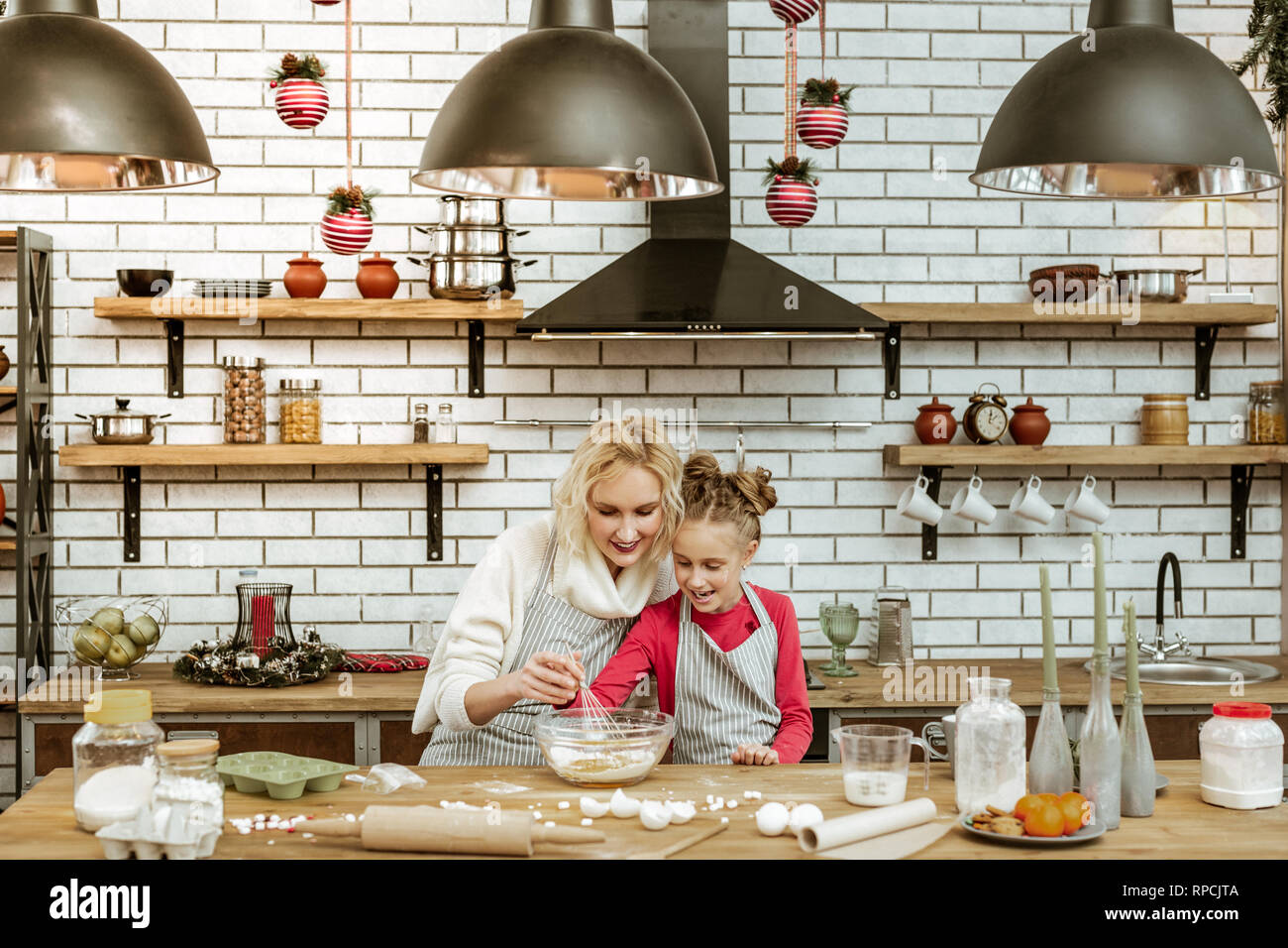 Smiling blonde lady sitting with daughter in stylish filled kitchen Stock Photo