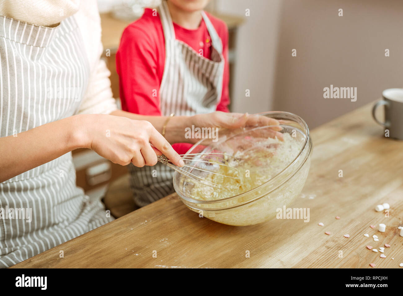Active mother in striped apron displaying way of working with whisk Stock Photo