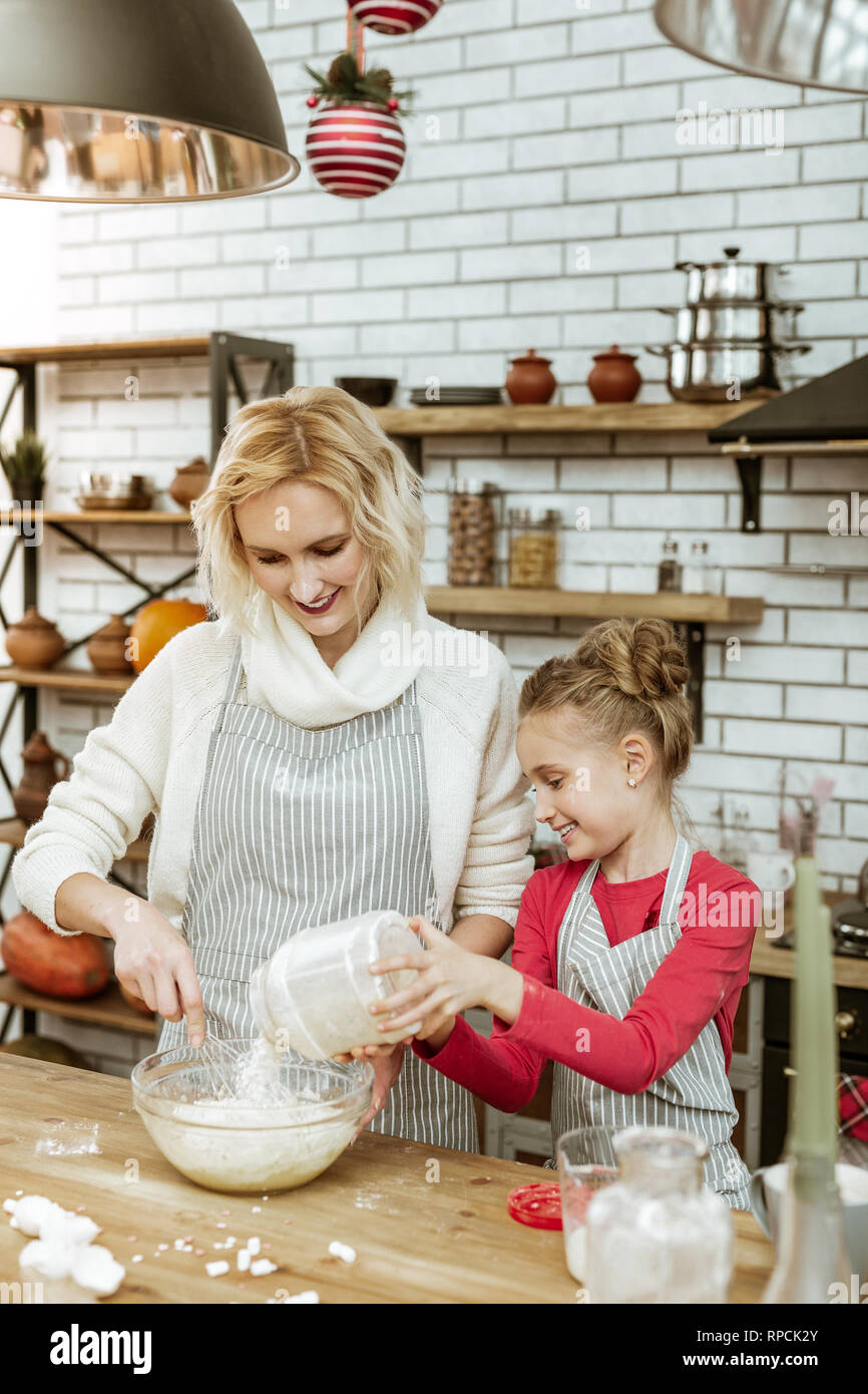 Beaming short-haired woman mixing dough while daughter helping Stock Photo