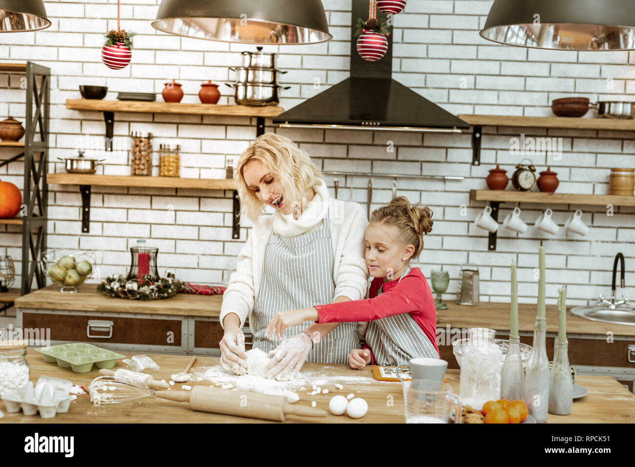 Joyful little kid in red dress sifting flour on dough piece Stock Photo