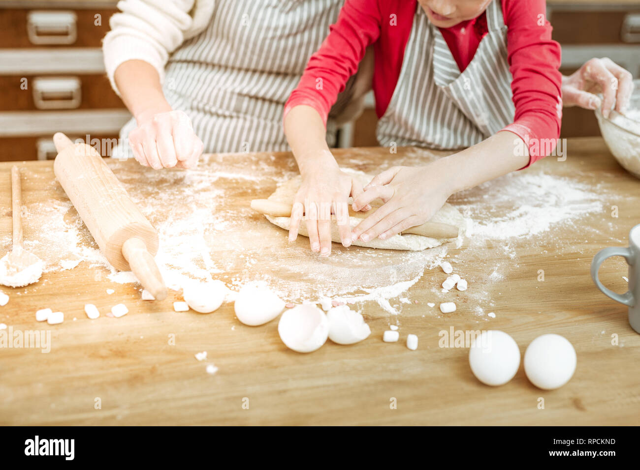 Attentive little child in red dress using little wooden rolling pin Stock Photo