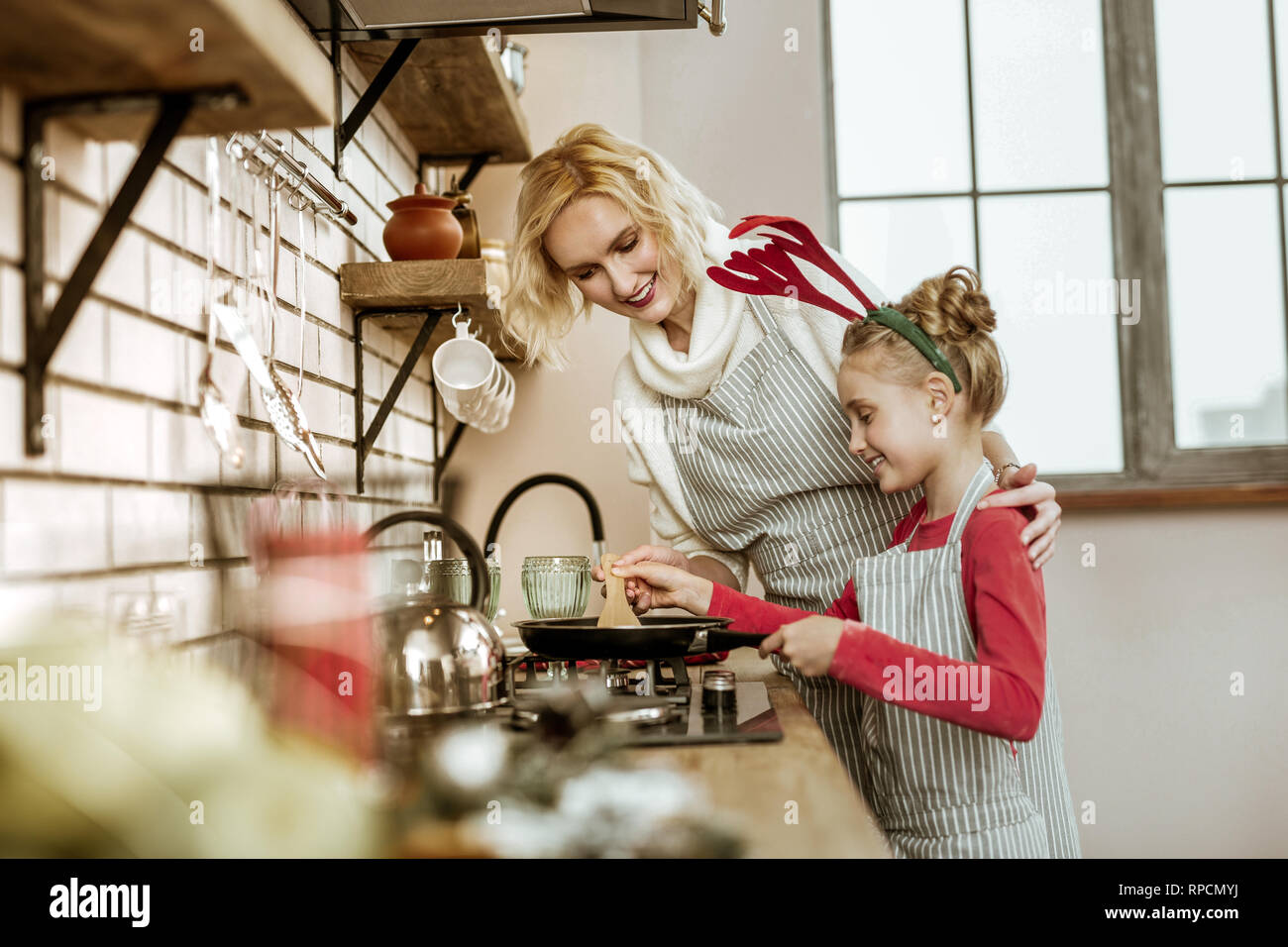 Smiling blonde mother and her beaming daughter standing nearby Stock Photo